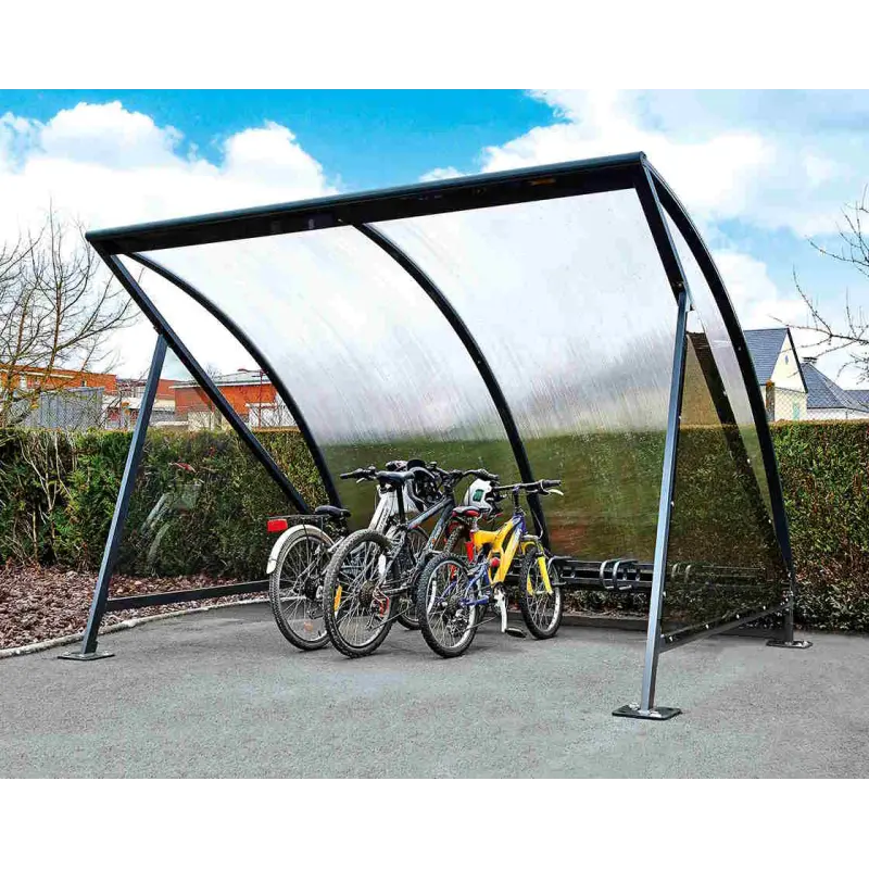 Wetterfeste Fahrradüberdachung Halbmond mit transparentem Dach und Fahrradständer auf einem asphaltierten Parkplatz vor Hecken.