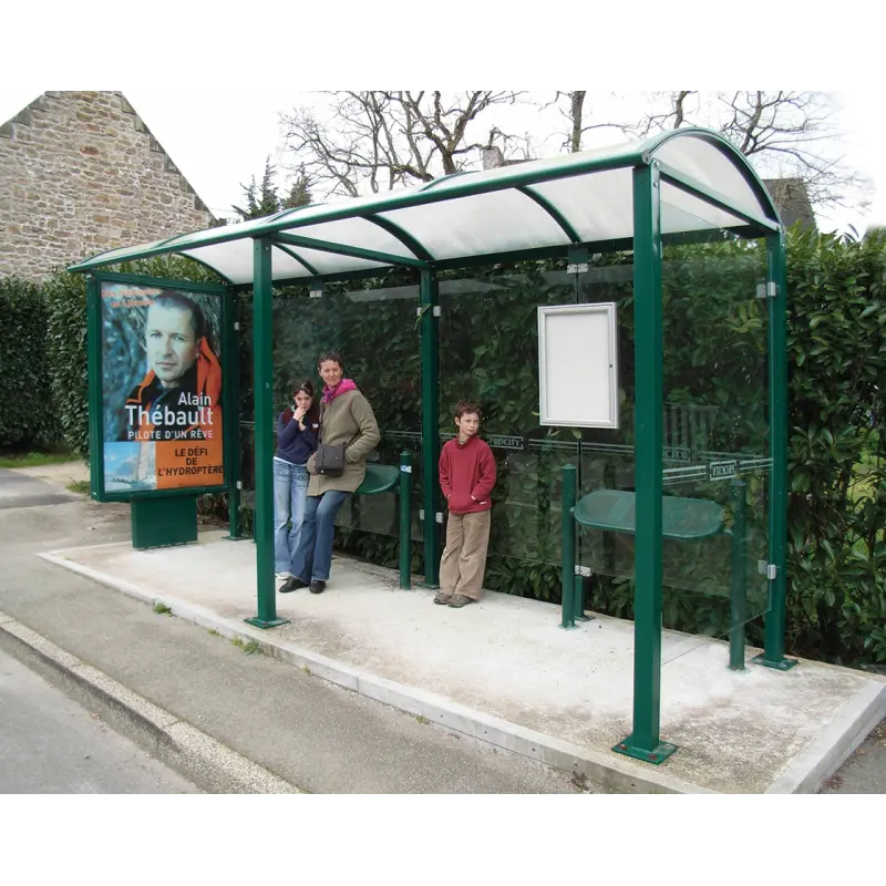 Grüne Standlehnen Estoril Agora montiert in einem Fahrgastunterstand an einer Bushaltestelle mit wartenden Fahrgästen.